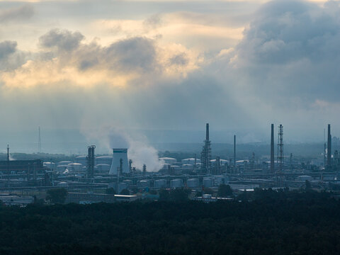 SchwedtOder, Germany - 20 August 2026: Aerial view of PCK Raffinerie GmbH oil refinery with industrial chimneys, cooling towers, and storage tanks under a cloudy sky with sunbeams.