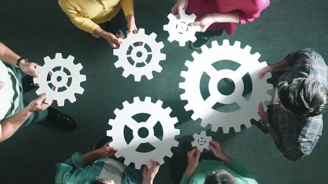 Top down aerial view of business team working together to gather cog together. Aerial view of professional diverse group holding cog and complete white gear. Represented unity, teamwork. Symposium.