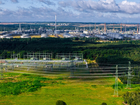 Schwedt Oder, Germany - 20 August 2026: Aerial view of PCK Raffinerie GmbH oil refinery with storage tanks, industrial infrastructure, and power lines, set against green forests and fields.