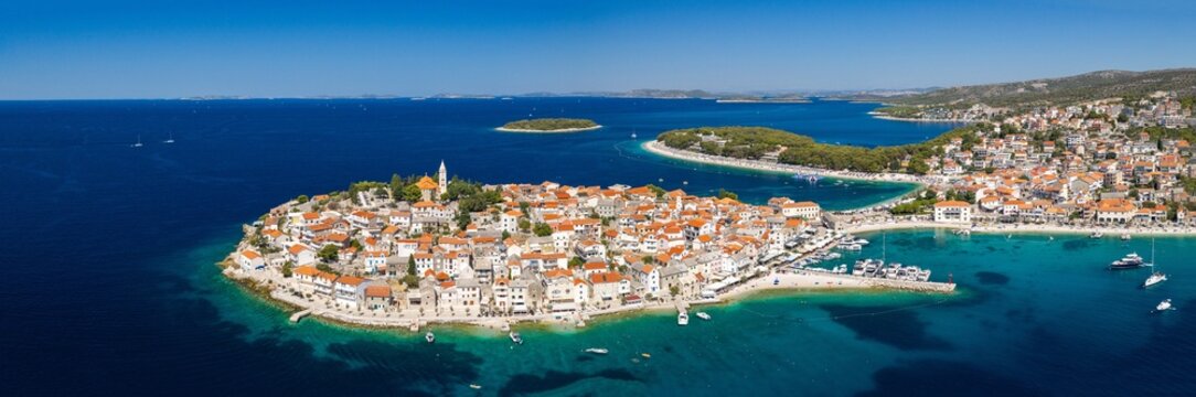 Aerial panoramic view of Primo&scaron;ten, Croatia, showing the historic peninsula, red rooftops, turquoise Adriatic waters, beaches, marina, surrounding islands and rugged Mediterranean coastline.