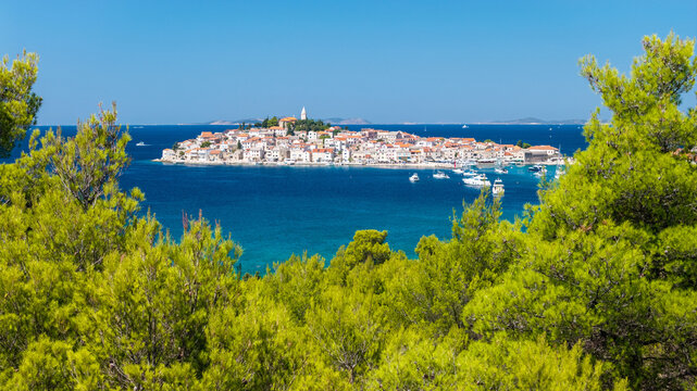 Panoramic view of Primo&scaron;ten, Croatia, framed by Mediterranean trees, with the historic old town, red rooftops, church tower, turquoise Adriatic Sea, yachts and distant islands.