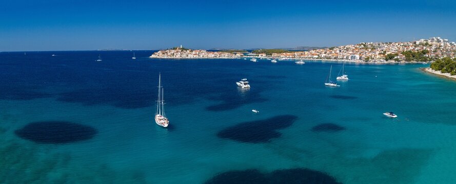 Aerial panoramic view of Primo&scaron;ten, Croatia, showing the historic coastal town, red rooftops, turquoise Adriatic waters, yachts, sandy beaches, Mediterranean architecture and sunny summer scenery.