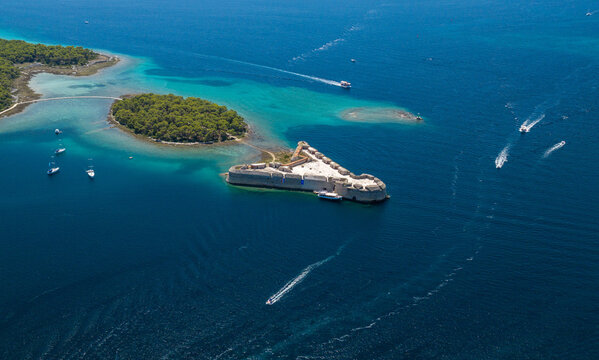 Aerial view of St. Nicholas Fortress near &Scaron;ibenik, Croatia, surrounded by turquoise Adriatic waters, forested islands and boats leaving trails across the sea on a sunny summer day.