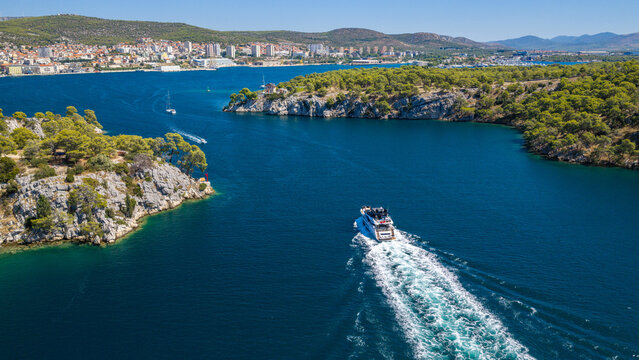 Aerial view of &Scaron;ibenik, Croatia, with a luxury yacht cruising through a scenic Adriatic channel, rugged pine-covered coastline, blue waters and the city skyline in the background.