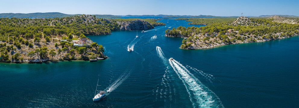 Aerial view of Luka Channel near &Scaron;ibenik, Croatia, featuring rugged pine-covered islands, deep blue Adriatic waters, rocky coastline and boats creating dynamic wakes across the channel.