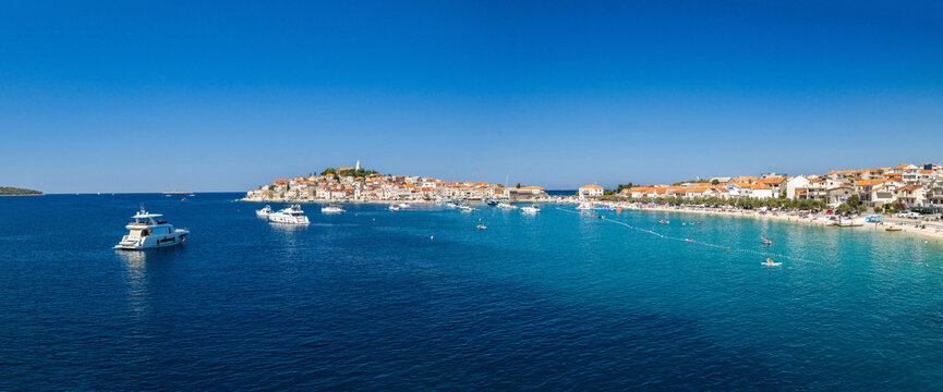 Aerial panoramic view of Primo&scaron;ten, Croatia, showing the historic coastal town, red rooftops, turquoise Adriatic waters, yachts, sandy beaches, Mediterranean architecture and sunny summer scenery.