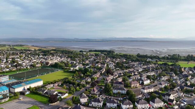 Wide panoramic aerial drone video over Tain town showing sports pitches, stone houses, and Dornoch Firth bay