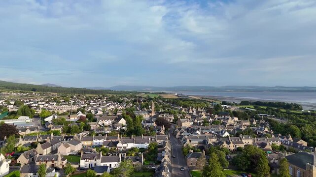 Establishing aerial drone shot flying forward over Tain town center toward Tolbooth tower and Dornoch Firth
