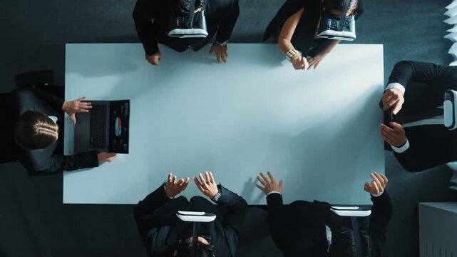 Top down aerial view of diverse data analysts wearing VR headset and stand around table while using hand gestures to manipulate the data streamed live from executive manager's laptop. Directorate.