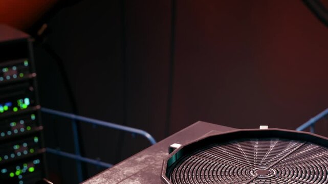A circular device sits on a table in a room with dim lighting. Behind it, there are several electronic units with lights. This scene displays a technical setup in a lab.