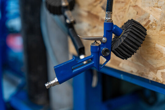 Blue pneumatic industrial tool rests against plywood and shows air connector, silver lever, and ribbed rubber wheel. Soft background blur keeps attention on rugged workshop hardware and compact mount.
