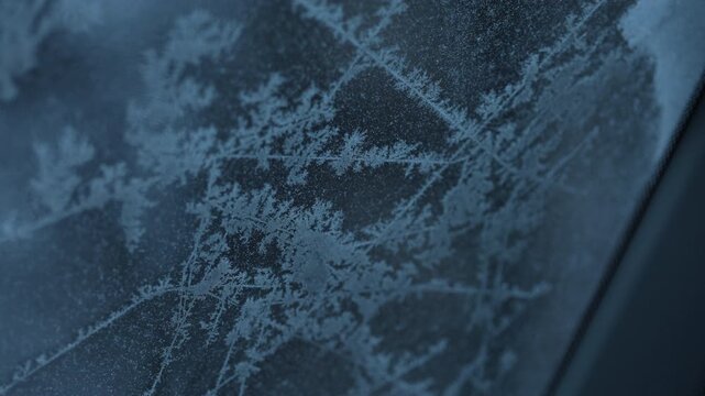 Macro close-up of frost crystals forming icy patterns on cold glass, cinematic blue tones, shallow depth of field, winter texture background.  ideal for winter, nature, weather, and abstract 