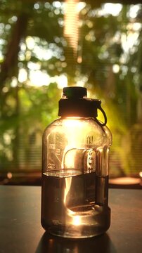A plastic water bottle gleams in warm sunlight against a blurred green background. Concept encompasses hydration, eco-friendliness, outdoor activities, and summer energy.