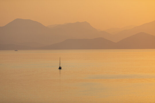 Silhouette of a sailboat on the open sea in the orange glow of the setting sun.