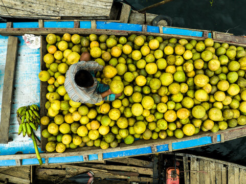 Rangamati Hill District, Bangladesh - 30 September 2023: Aerial view of a person sitting on a wooden boat filled with yellow pomelos on Kaptai Lake.