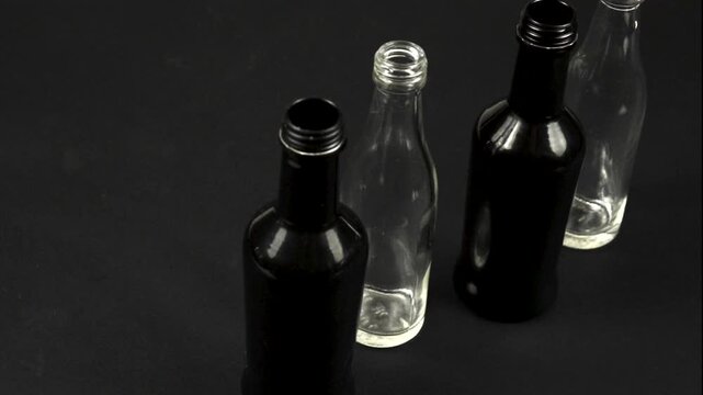 Glass black, white bottles stand on a black background, versatile containers used for storage of different objects and liquid. Glass bottles collection, side view, slow motion