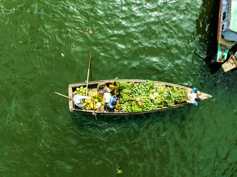 Rangamati Hill District, Bangladesh - 30 September 2023: Aerial view of a wooden boat loaded with fresh produce and fruits on the green waters of Kaptai Lake with local farmers navigating.
