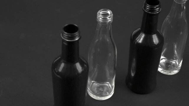 Glass black, white bottles stand on a black background, versatile containers used for storage of different objects and liquid. Glass bottles collection, side view, slow motion