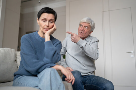 Hysterical egoistic elderly husband accusing and provoking upset older wife during family quarrel at home, irritated man gesturing and talking to stressed senior woman, aged couple relationship crisis