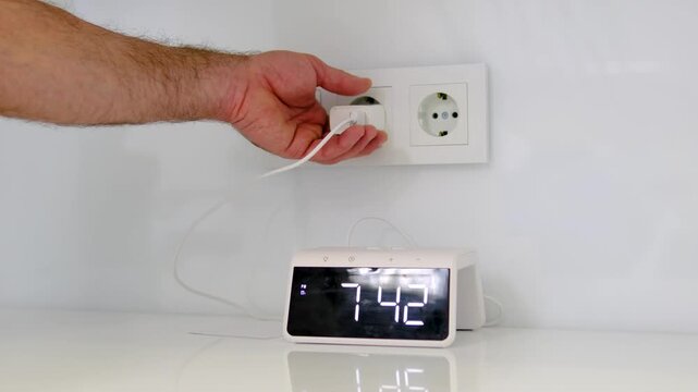 Male hand unplugging digital clock showing 7 42 from double wall outlet in home interior saving electricity close up everyday routine video