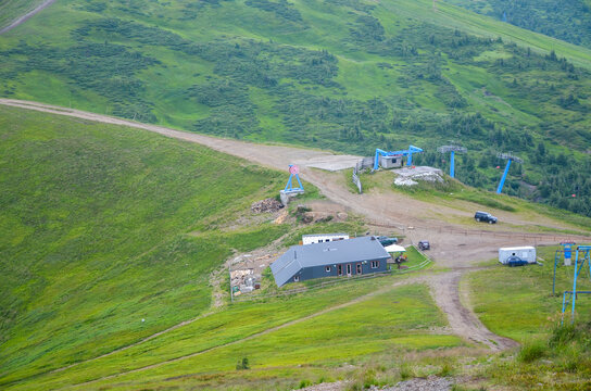 High angle summer view of Dragobrat, Ukraines highest ski resort, showing a chairlift station on Mount Stig, a winding dirt road, and vibrant green mountain ridges under an overcast sky