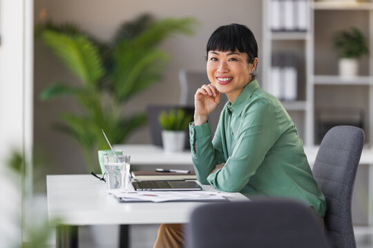 Smiling professional woman working at desk in modern bright office with laptop and documents