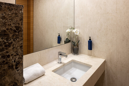 Close up of modern bathroom sink vanity with marble wall mirror and white towel