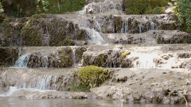 Scenic view of Bigar waterfall cascading over mossy tufa rock steps in a dense forest near Kalna, Stara Planina, Serbia. Cinematic pure nature stream footage shot in summer.
