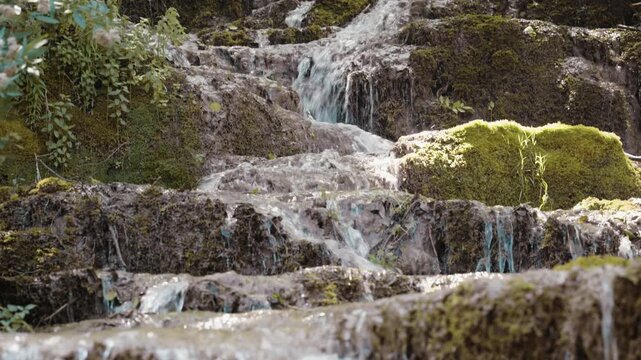 Scenic view of Bigar waterfall cascading over mossy tufa rock steps in a dense forest near Kalna, Stara Planina, Serbia. Cinematic pure nature stream footage shot in summer.