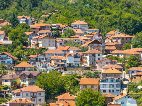 Aerial view of Vevchani village featuring traditional houses with orange tiled roofs nestled among lush green trees on a hillside in Vevchani, Vevcani Municipality, North Macedonia.