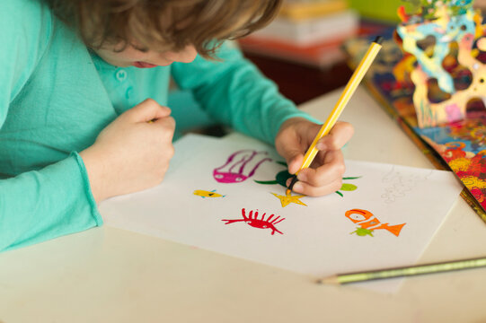 Close-up side view of a young boy sitting at a table drawing
