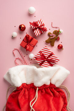 Santa Claus presents in a red velvet sack with striped gifts, candy cane and gingerbread for Merry Christmas and Happy New Year on vertical pastel pink background