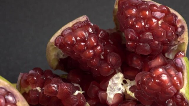 Close up view of fresh pomegranate seeds and fruit pieces, showing glossy red arils and pale inner membranes arranged closely together on dark surface