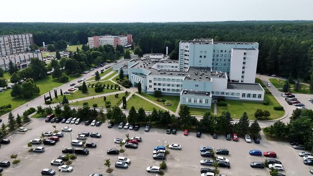 Klaipėda Seamen&rsquo;s Hospital complex and surrounding parking lots sit beside a forested residential district in daytime drone view.