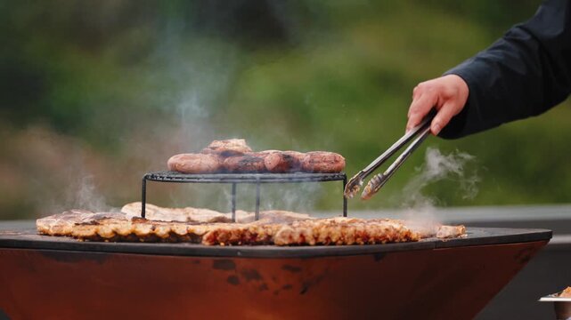 Tongs lift a piece of grilled pork from a smoking steel plancha loaded with meat