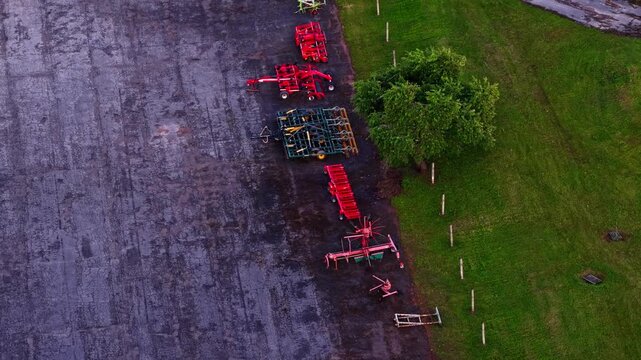 Top-down aerial view of various farm equipment and machinery parked in a row on the pavement