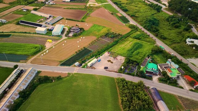 Aerial view over patchwork farm plots, ponds and teal-roofed farmhouses connected by rural roads near coastline in Gangneung, Gangwon-do
