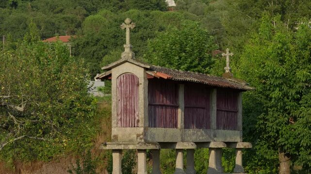 Espigueiro raised on stone pillars with wooden slats and carved crosses among green hillside trees