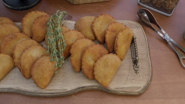 Golden half moon pastries lined up on a rustic wooden board garnished with thyme