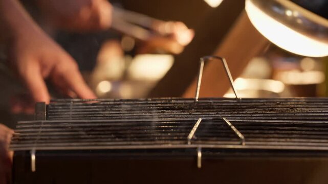 Bare grill grate steaming above a charcoal barbecue while a cook works out of focus behind