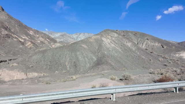 Precordillera of San Juan, Argentina with barren rocky mountains beside a roadside guardrail, outside from car window pov