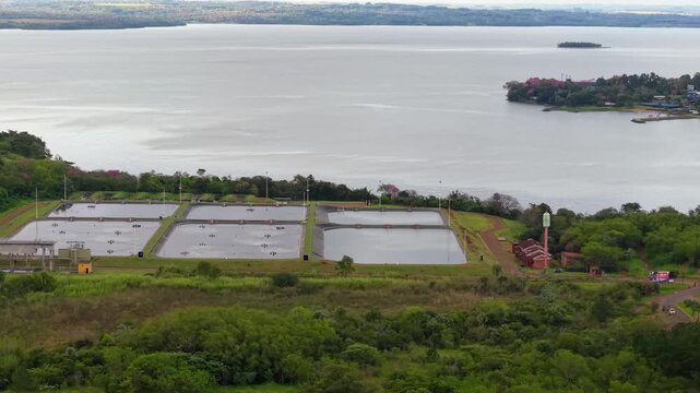 Wastewater treatment ponds sit beside the Parana River, Posadas, Misiones, Argentina, with Arroyo Martires nearby, captured in a lateral drone slide.