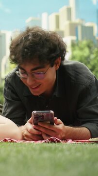 Vertical composition: Couple lies illustrating phubbing and phone addiction on a picnic blanket, focused on separate smartphones instead of each other, showing emotional distance and no communication.