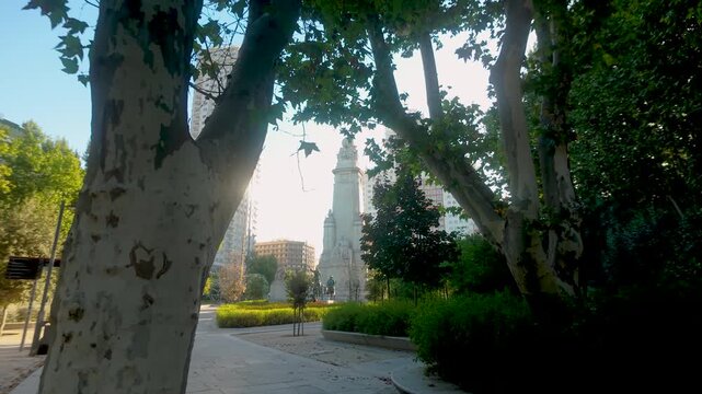 A view through plane trees of the Cervantes Monument in Plaza de Espana, Madrid, Spain. Suitable for travel documentaries and urban tourism content.