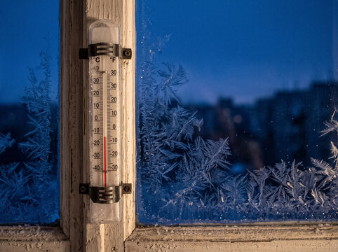 thermometer on wooden window frame shows minus twenty degrees against frosty patterns on glass