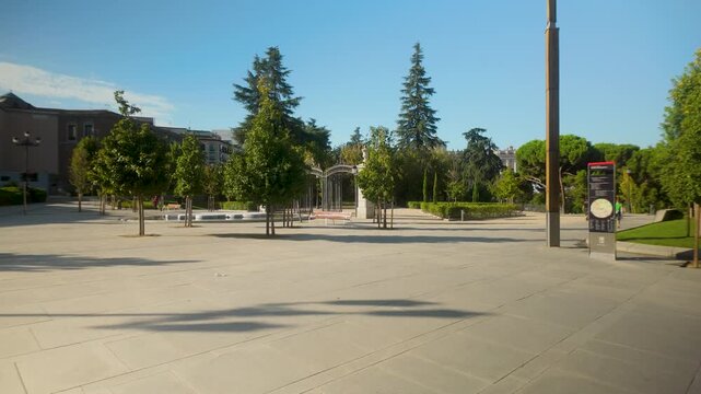 A wide shot of a peaceful urban plaza in Madrid featuring manicured trees and modern architecture under a clear blue sky. Useful for travel guides and urban planning content.