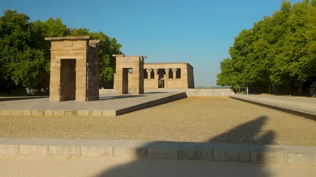 A wide shot of the Temple of Debod, an ancient Egyptian temple relocated to Madrid, Spain. Authentic historical landmark surrounded by lush greenery under a clear blue sky.