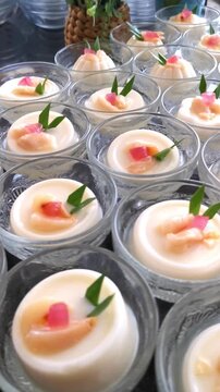 Vertical panning shot of Asian milk pudding desserts with lychee and pandan in glass bowls for catering banquet