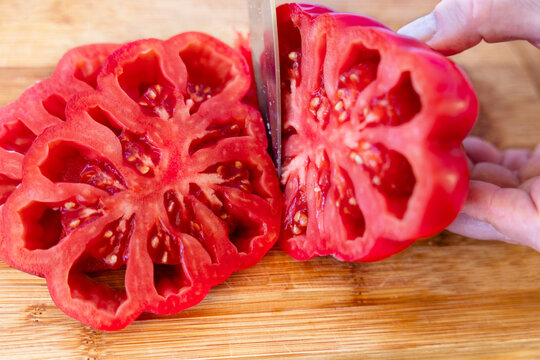 Slicing fresh ripe red beefsteak tomato on wooden board.
