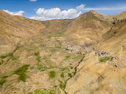 Aerial view of Chicham village nestled in the arid Himalayan mountains with terraced green fields and rugged terrain in Chicham, Himachal Pradesh, India.